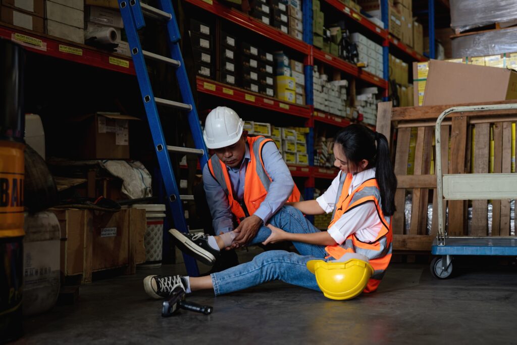 Mature foreman in workwear giving first aid to asian women staff.